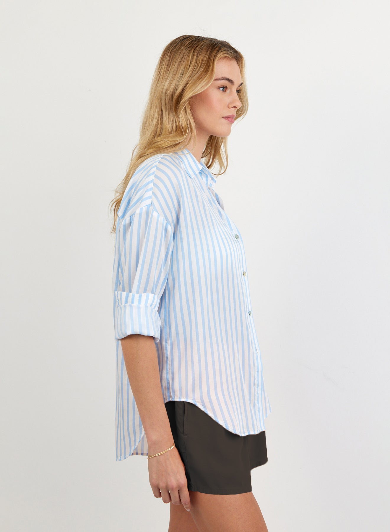 Woman wearing oversized blue striped button-down shirt with rolled sleeves and black shorts