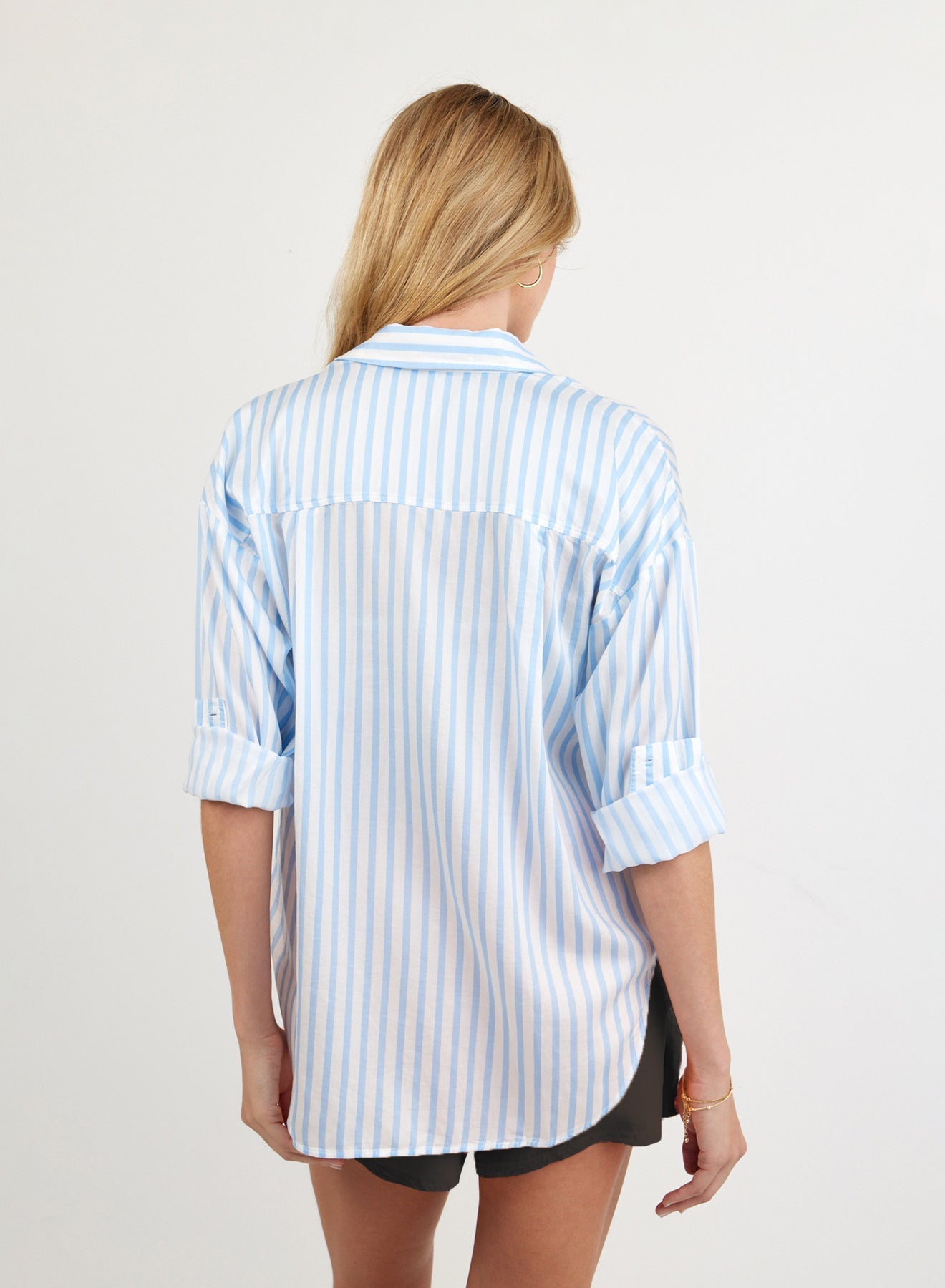 Woman wearing oversized blue and white striped button-down shirt, back view