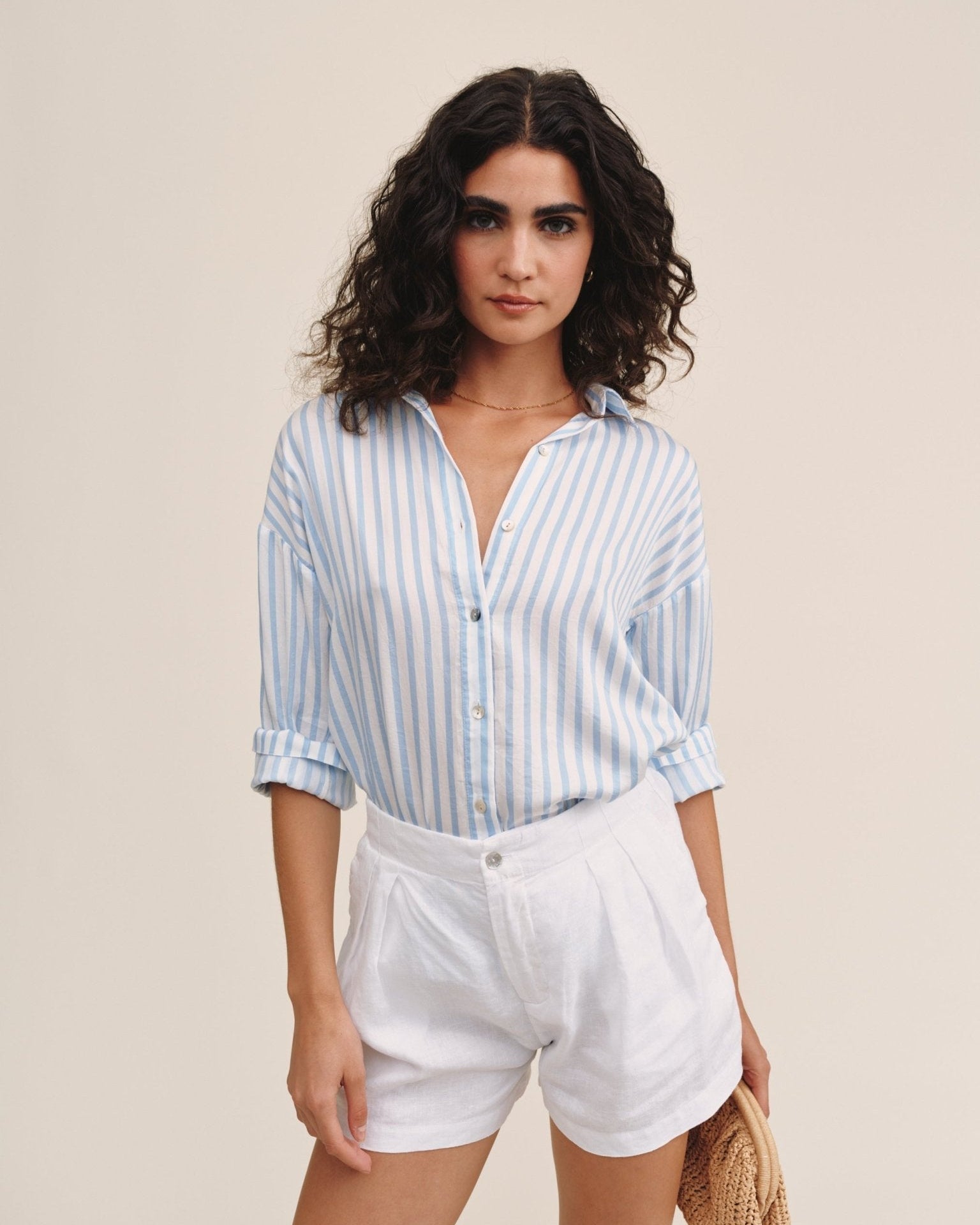 Woman wearing oversized light blue striped button-down shirt with white shorts