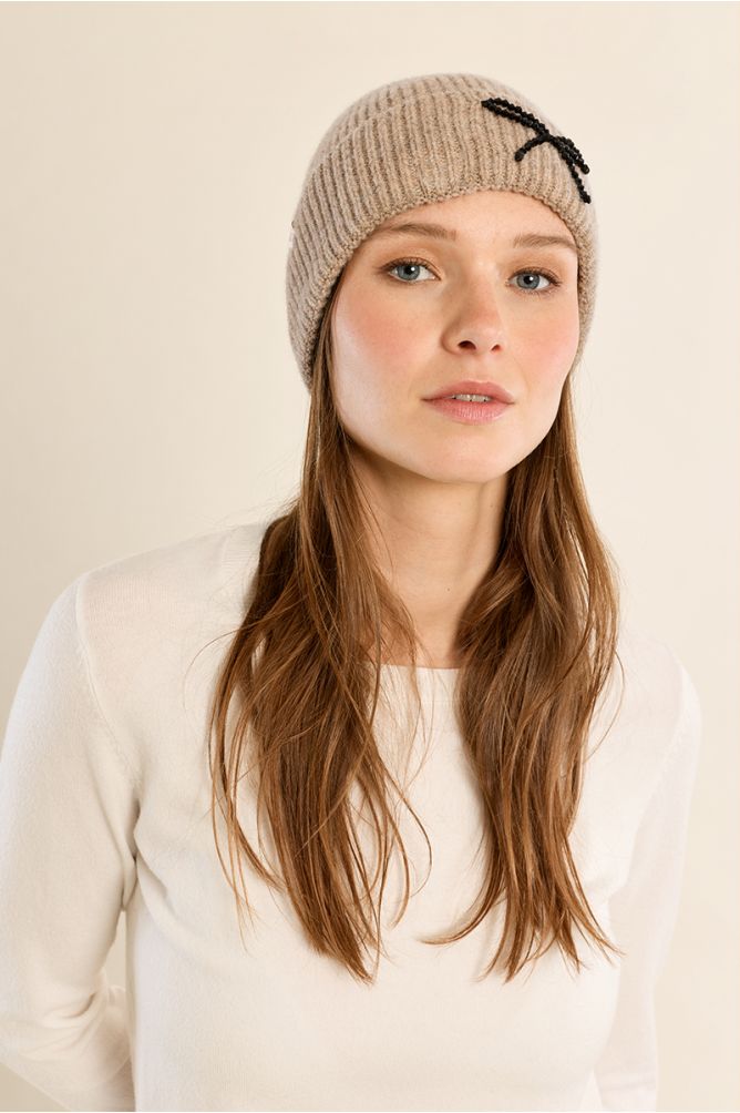 Woman wearing a beige ribbed knit beanie hat with black bow embellishment by Molly Bracken