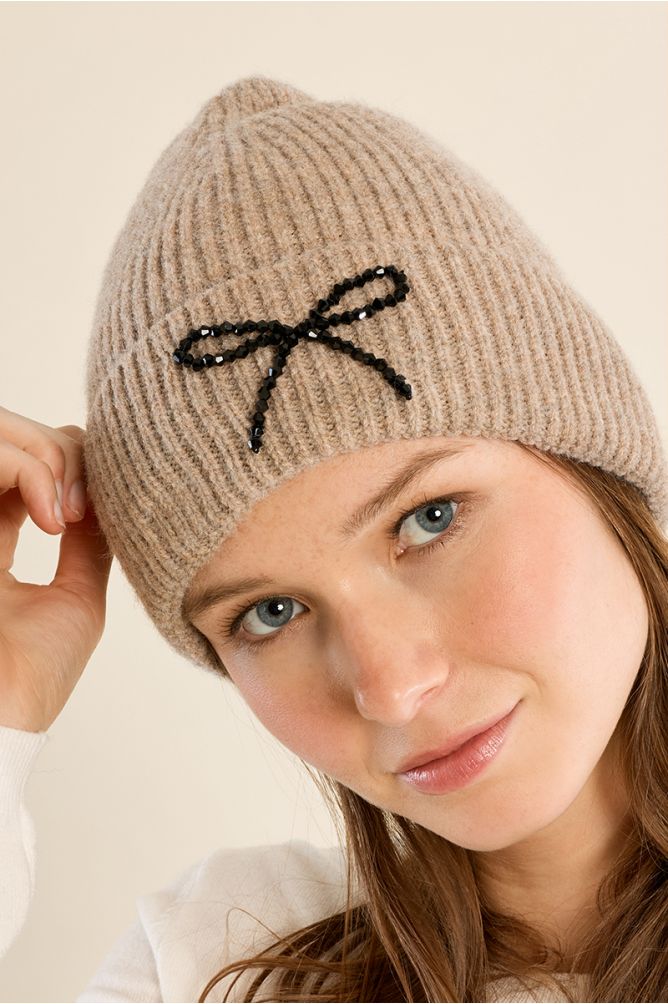Molly Bracken beige ribbed knit beanie hat with black beaded bow embellishment on model