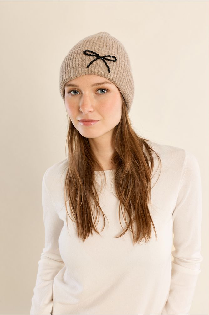 Molly Bracken beige knit beanie hat with black sequin bow detail on model