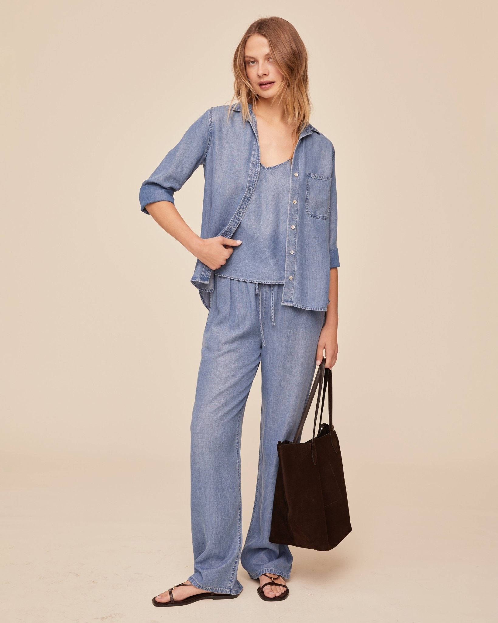 Woman wearing BELLA DAHL indigo denim button-down shirt with matching wide-leg pants and black bag