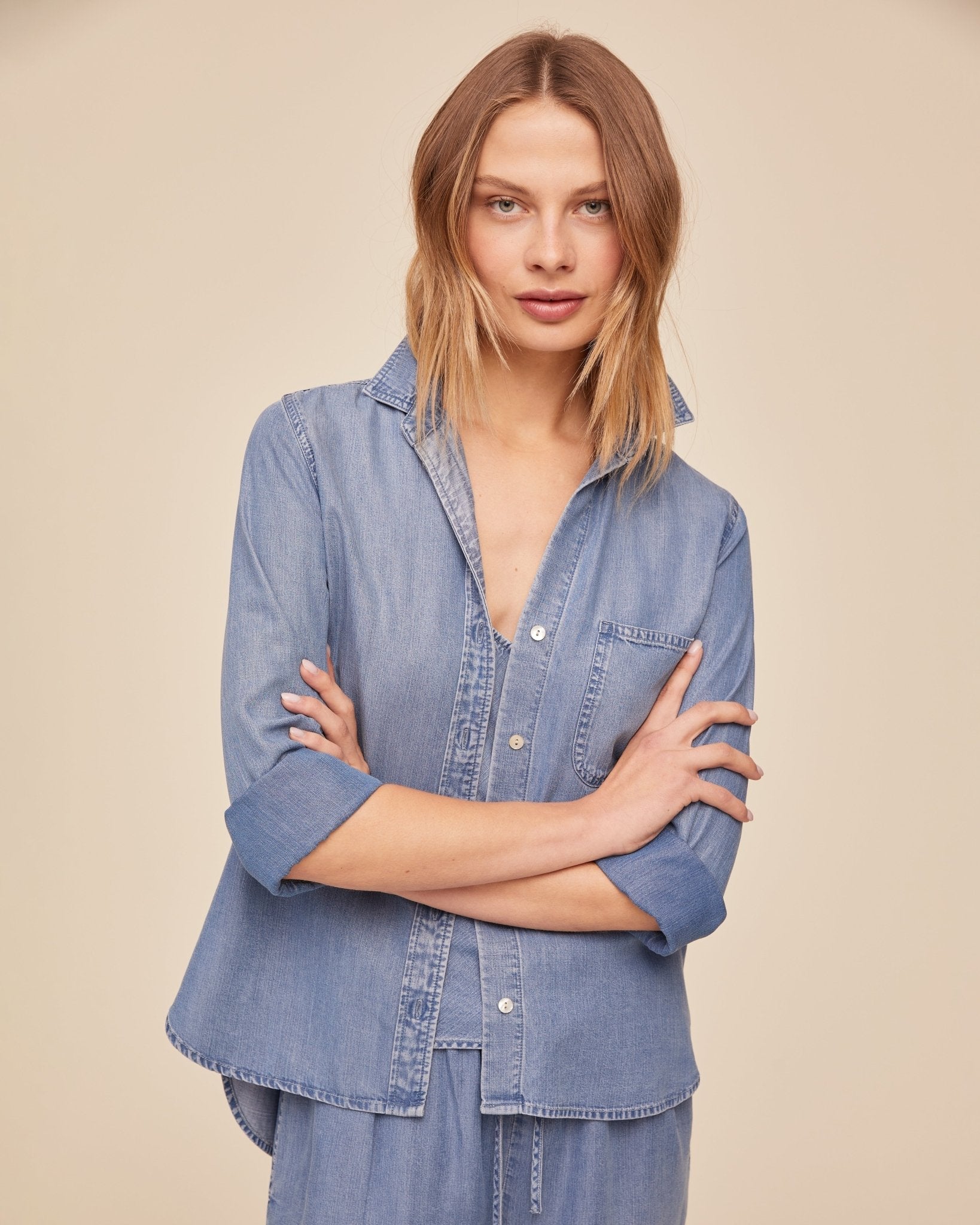 Woman wearing BELLA DAHL indigo denim button-down shirt with arms crossed, studio background