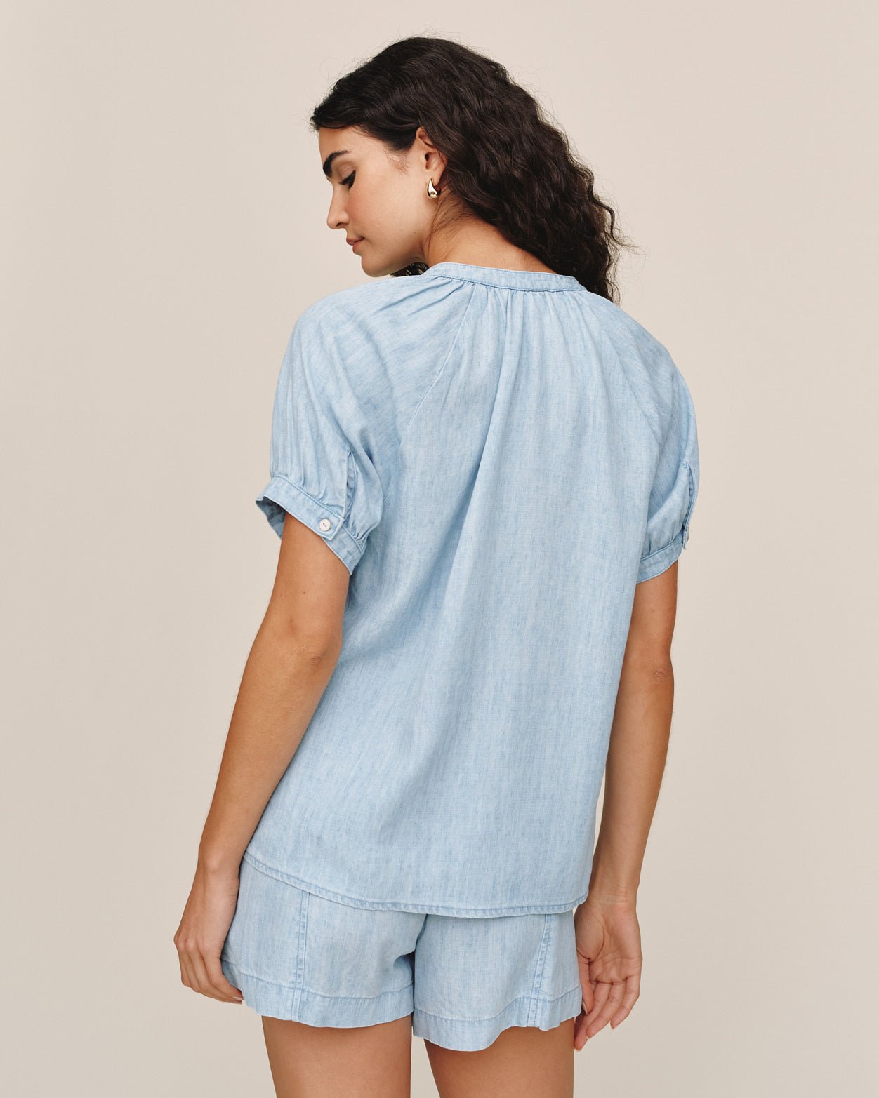 Woman wearing light blue chambray short sleeve raglan shirt and matching shorts, back view