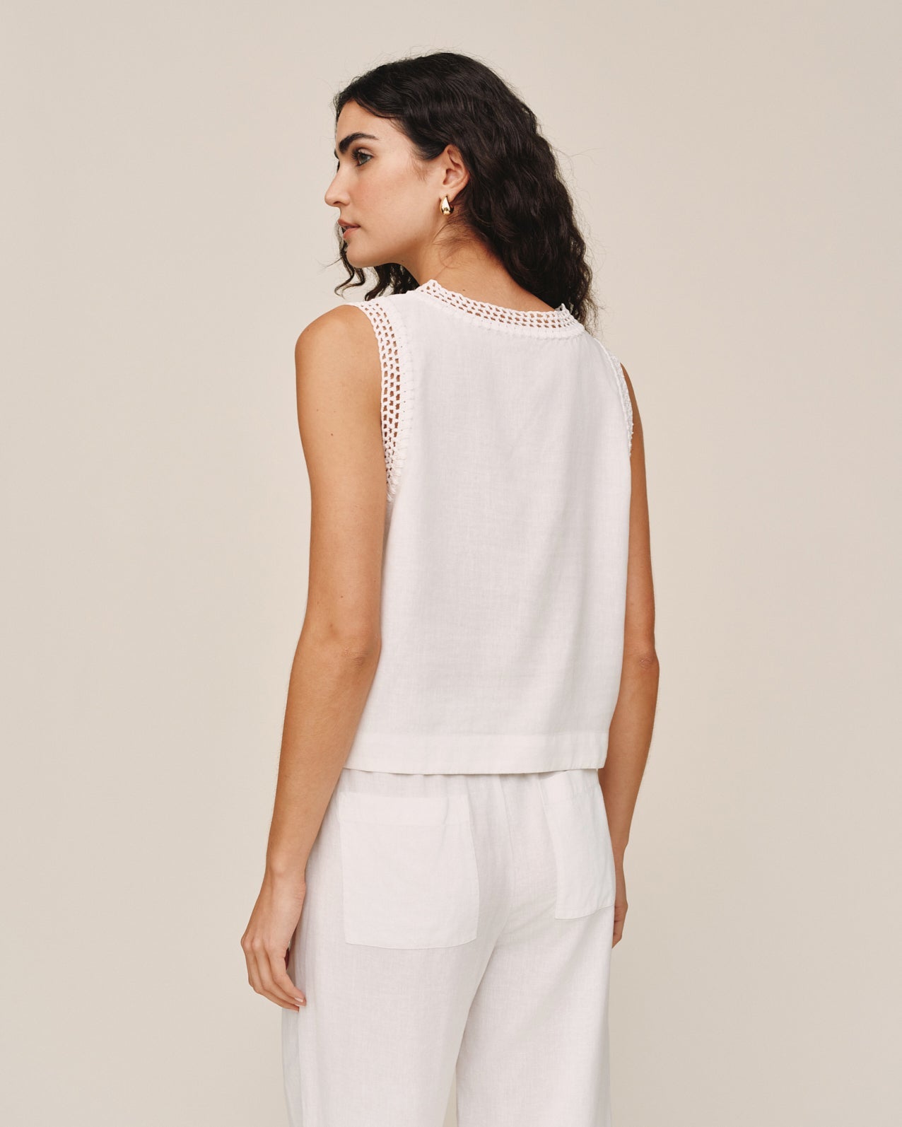Woman wearing ivory sleeveless top with crochet trim detail, shown from back view