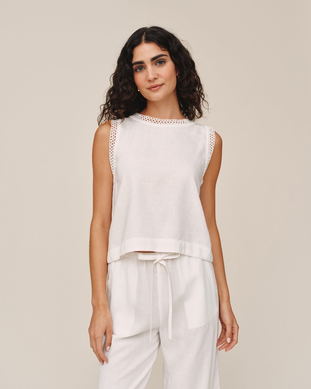 Woman wearing ivory sleeveless top with crochet trim details and matching drawstring pants