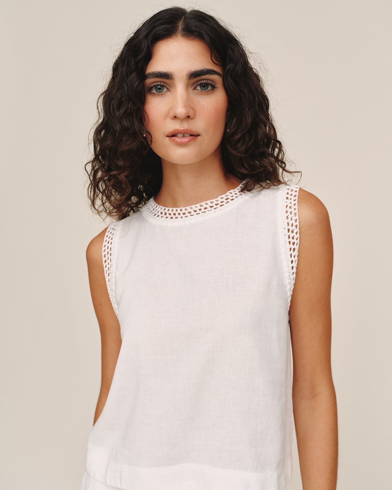 Woman wearing ivory sleeveless top with crochet lace trim detail at neckline and armholes