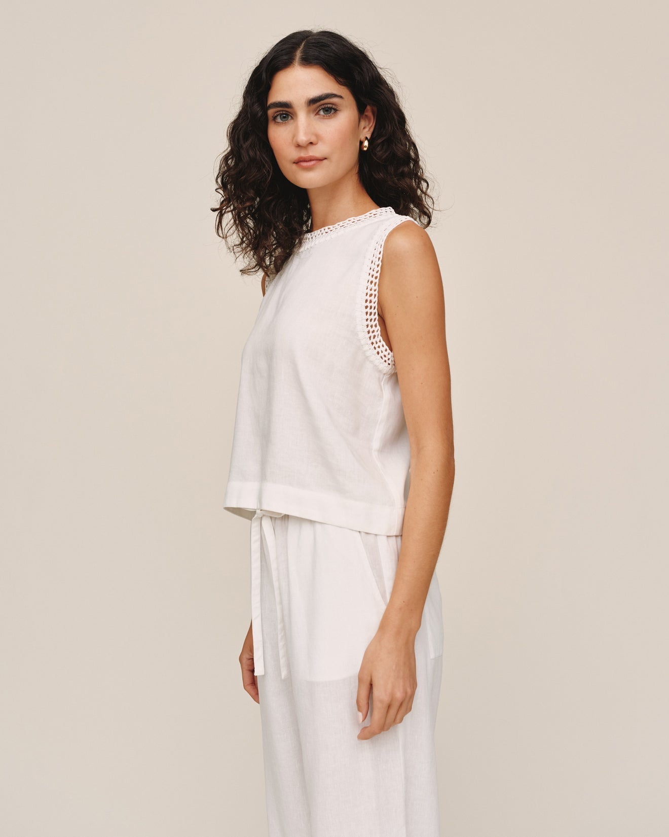 Woman wearing ivory sleeveless top with crochet edge details and matching drawstring pants