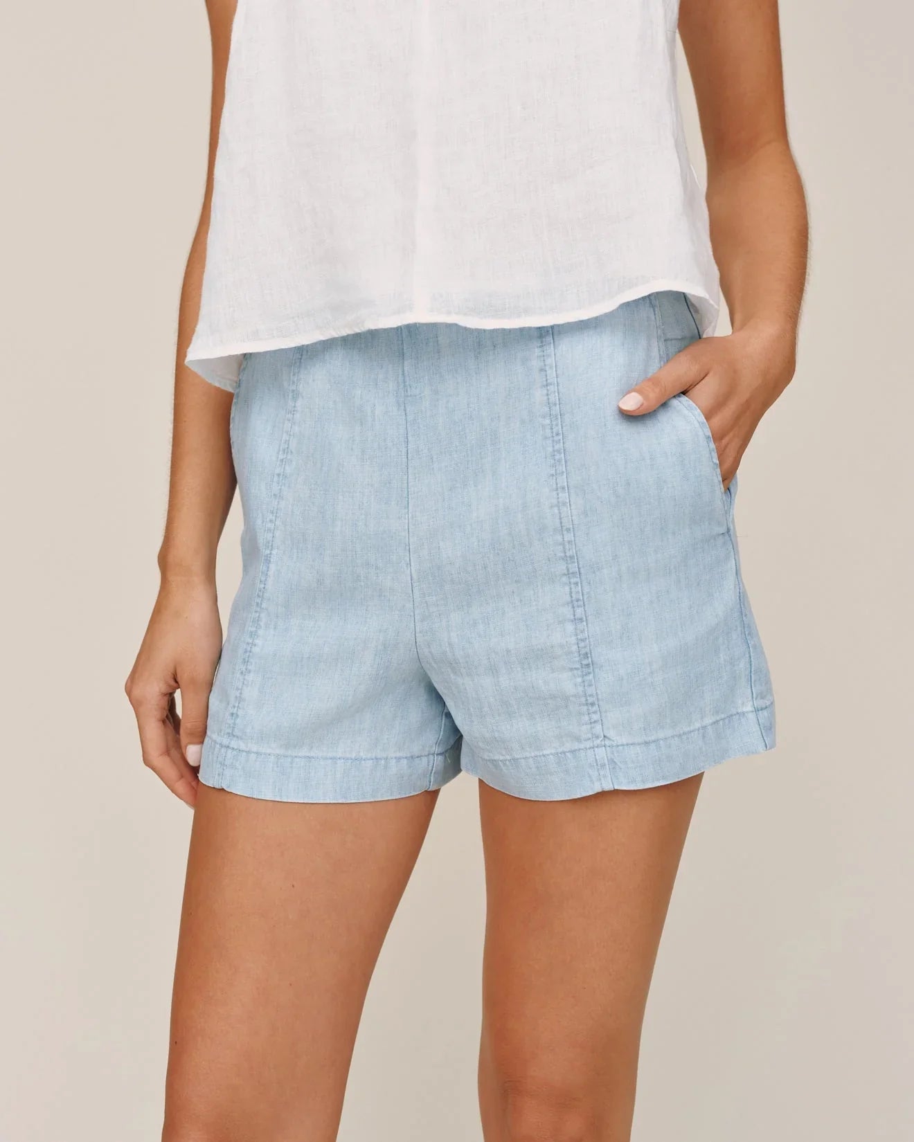 Light blue denim shorts with rolled cuffs and smocked waistband worn with white tank top