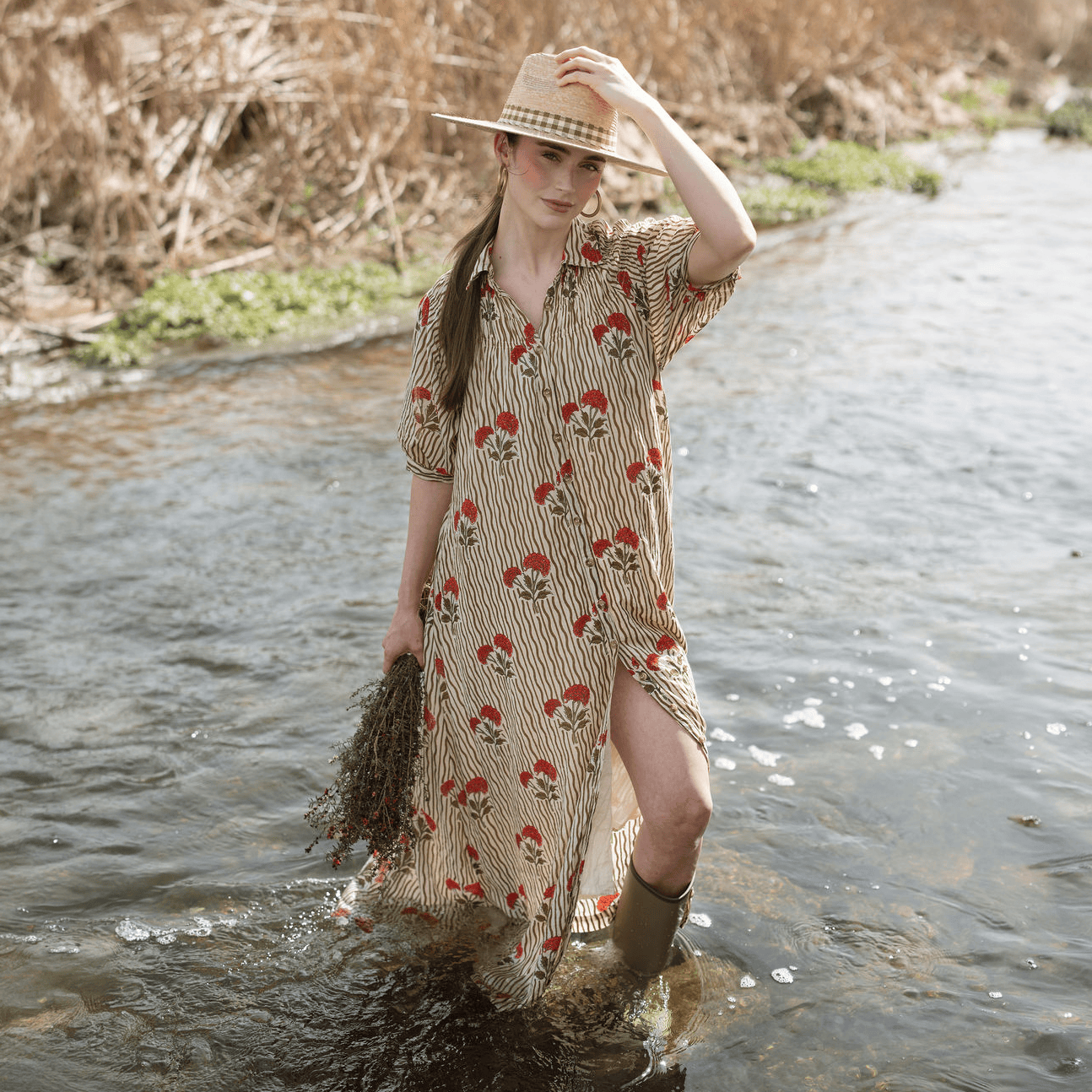 Woman wading in stream wearing Sunshine Tienda Wavy Stripe Oasis Dress with straw hat and rain boots